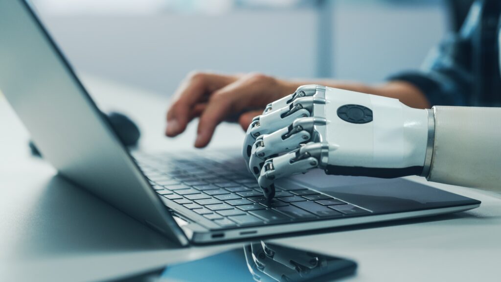 Human hand and robotic hand typing together on a laptop, representing collaboration between artificial intelligence and Lean Six Sigma.