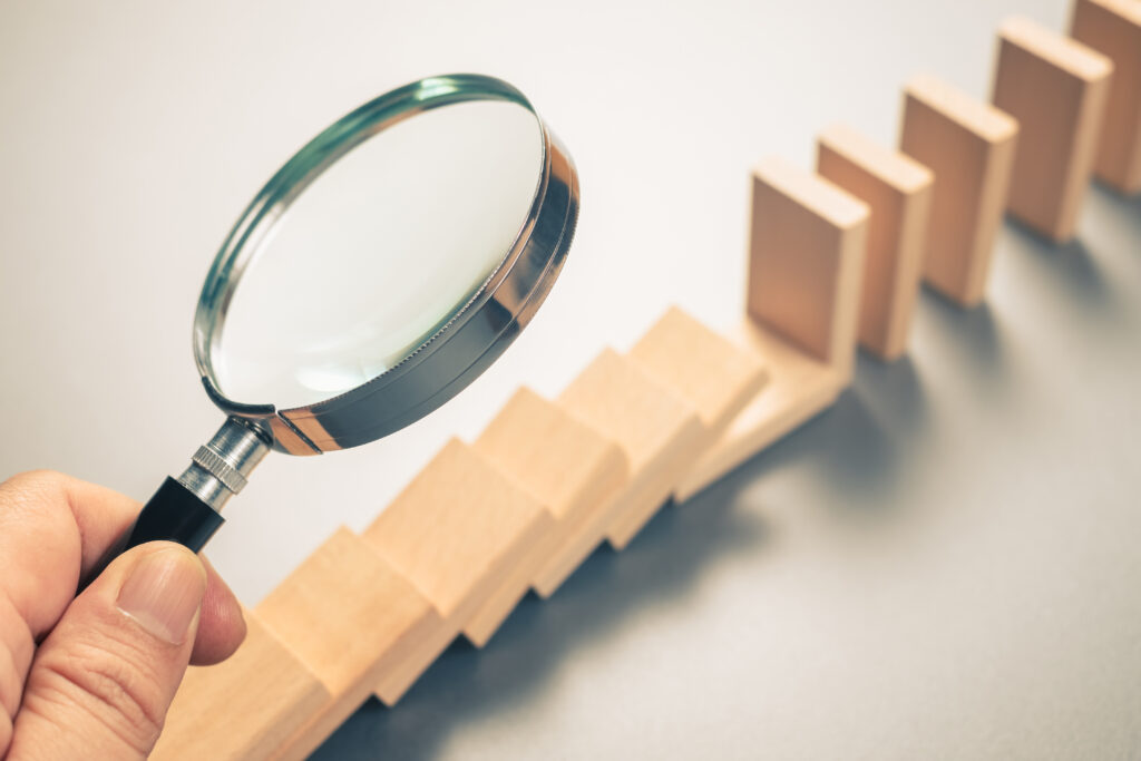 Photo of a hand holding a magnifying glass over a row of wooden blocks, illustrating a close examination of one part of a larger process.