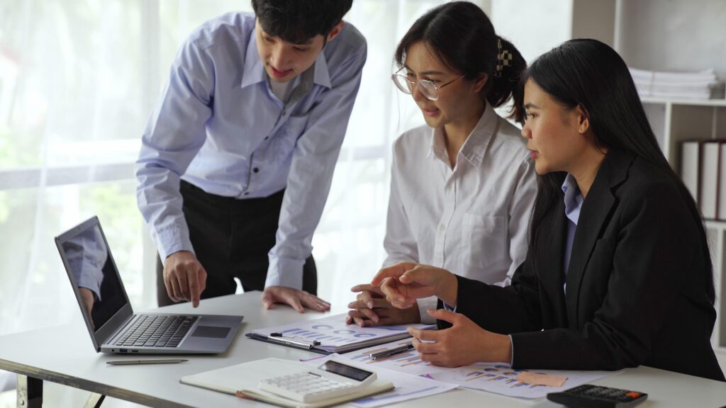 Three colleagues collaborating around a computer during an improvement project meeting, illustrating shoulder-to-shoulder communication and stakeholder collaboration.